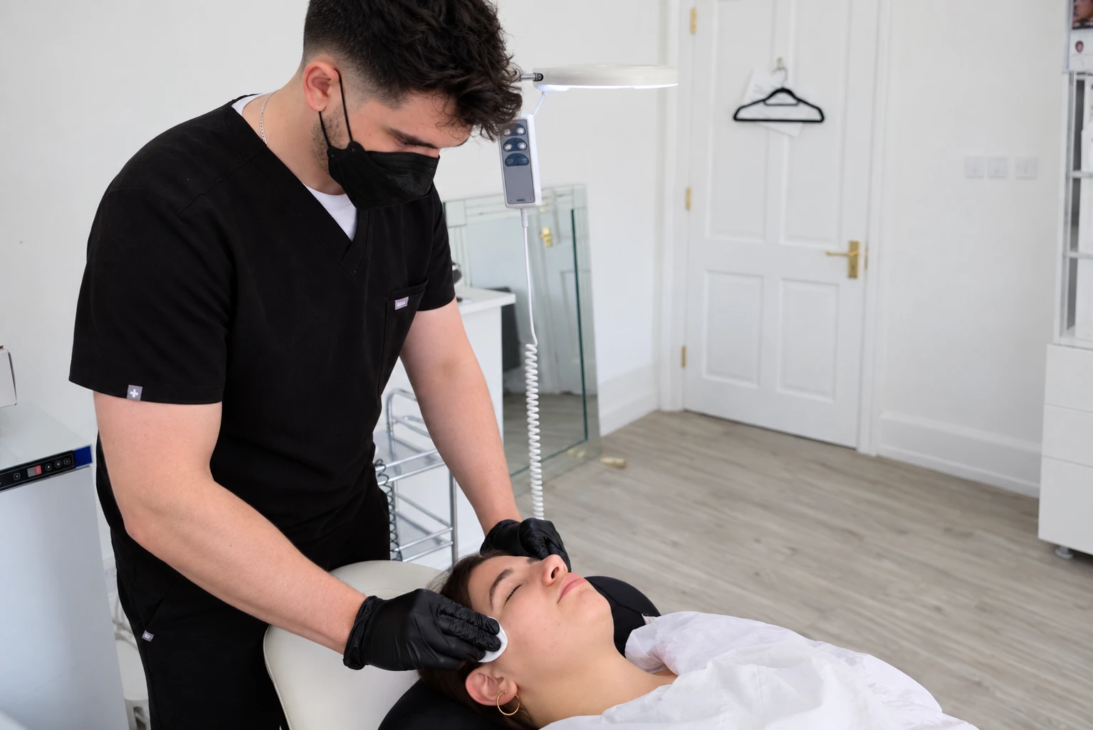 Dale wearing a mask and gloves while caring for a patient in an aesthetics treatment room