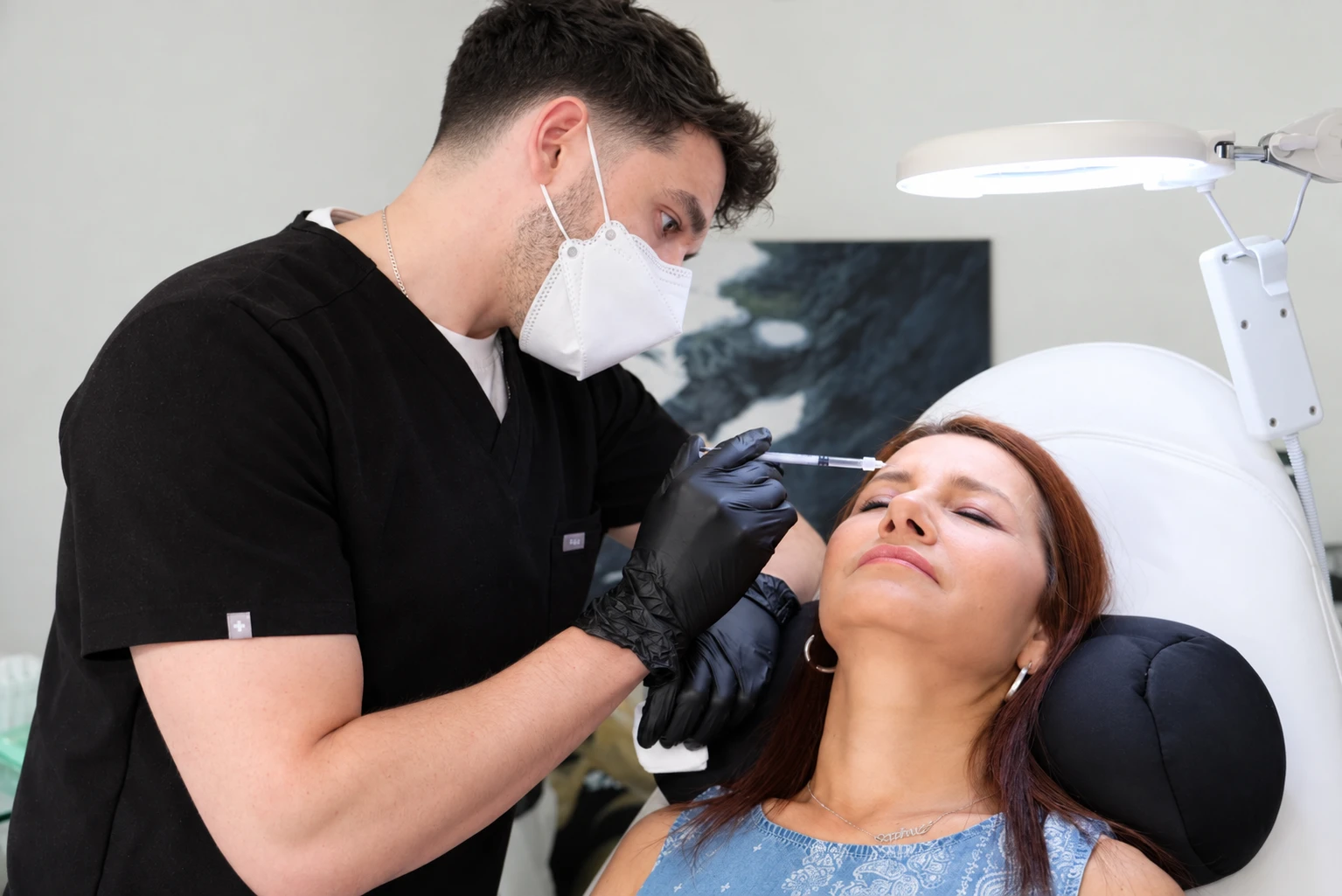 Dale wearing a mask and gloves while providing an aesthetic treatment in a clinical setting